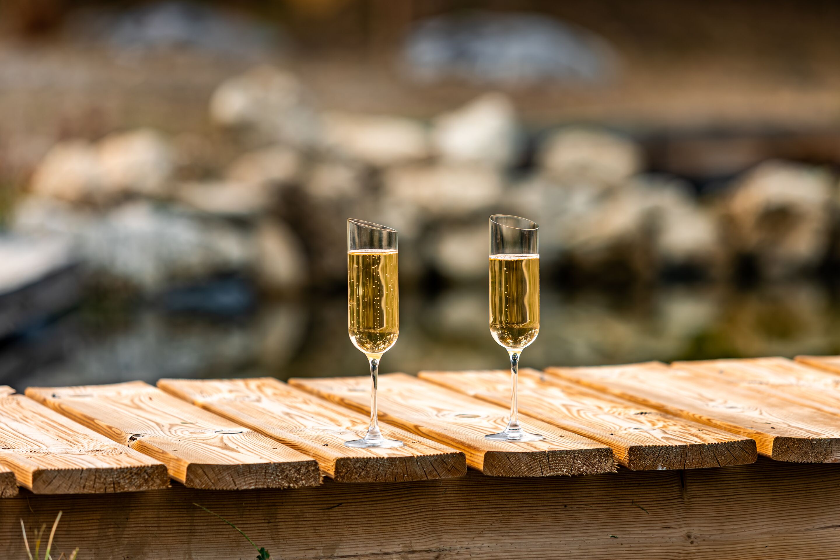 Deux coupes de champagne sur une table en bois, avec un arrière-plan naturel flou.