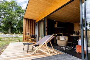 A wooden deck with a folding chair, a small table, and a sofa. - Pépites Lodges et Spas (Prémilhat)