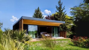 A modern house with a large glass window, a wooden deck, and a garden. - Pépites Lodges et Spas (Prémilhat)