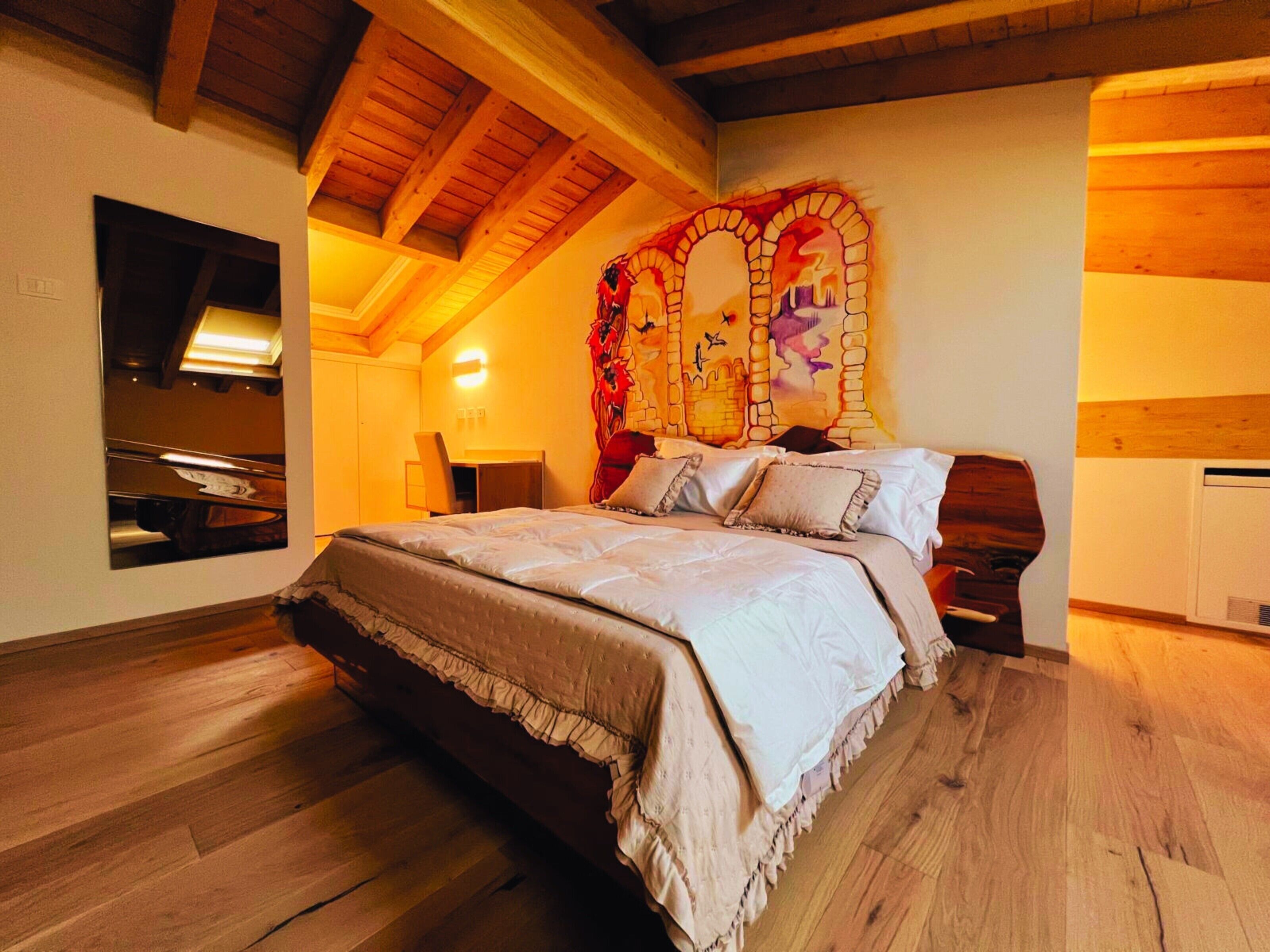 A bedroom with a large bed, wooden beams, a mirror, and a decorative wall piece.