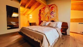 A bedroom with a large bed, wooden beams, a mirror, and a decorative wall piece.