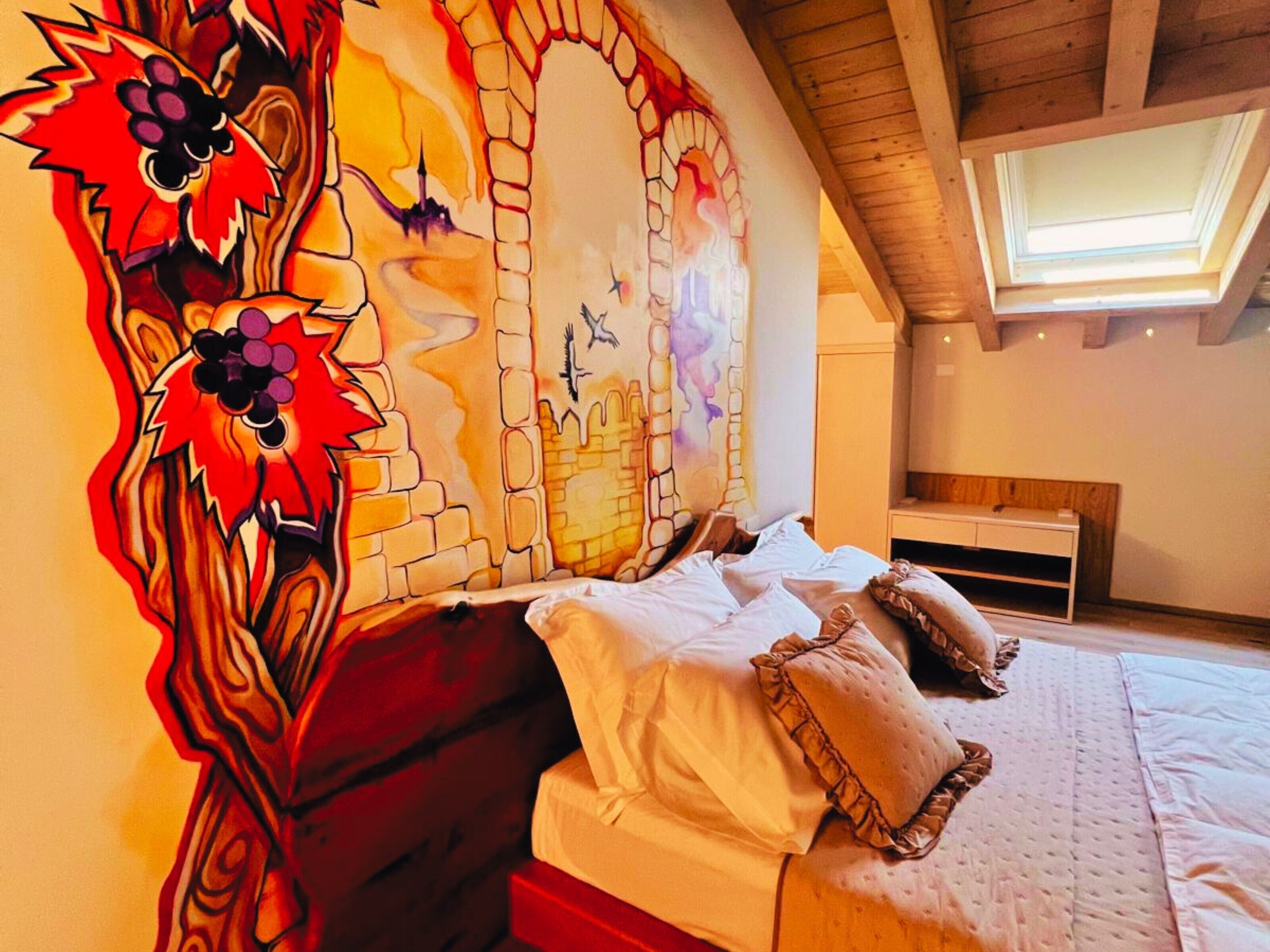 Une chambre avec un grand lit, une tête de lit en bois, une lucarne et une fresque murale.