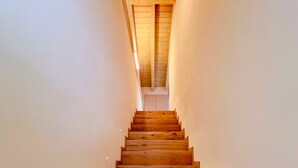 A wooden staircase leading to a loft bedroom with a sloped ceiling. - 45 m² Room with Private Bathroom – Up to 2 Guests (Illasi)
