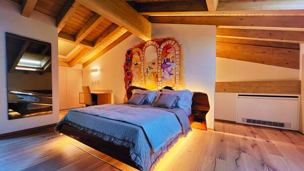 A bedroom with a sloped ceiling, wooden beams, a bed with a ruffled bedspread, a wall-mounted air conditioner, and a skylight. - 45 m² Room with Private Bathroom – Up to 2 Guests (Illasi)