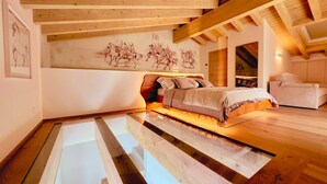 Un dormitorio con piso de vidrio, vigas de madera, una cama y un cuadro en la pared.