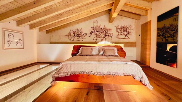 Un dormitorio con techo inclinado, vigas de madera, una cama grande y obras de arte con motivos de caballos en las paredes.
