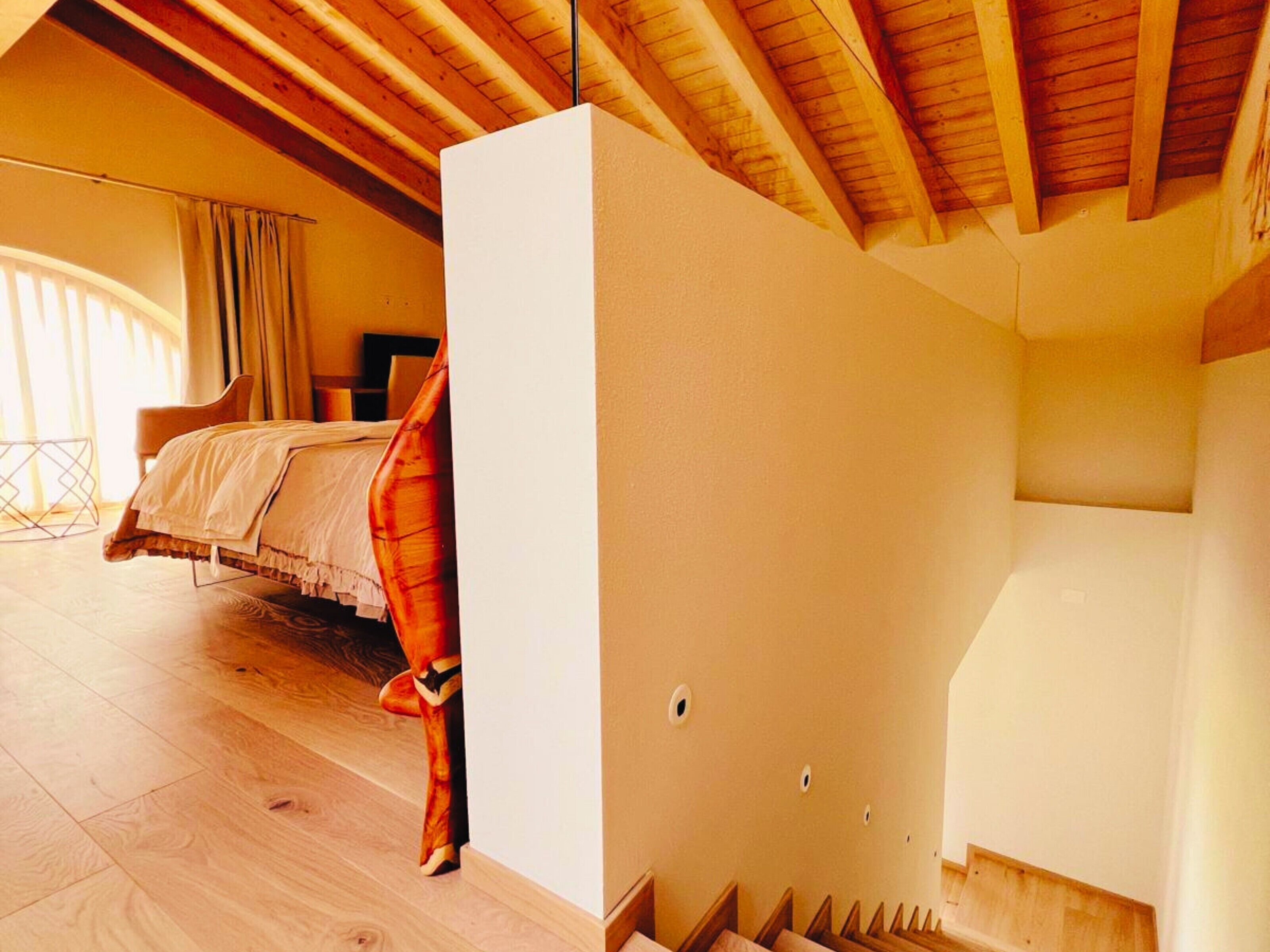 A bedroom with a bed, wooden ceiling beams, and a window with curtains.