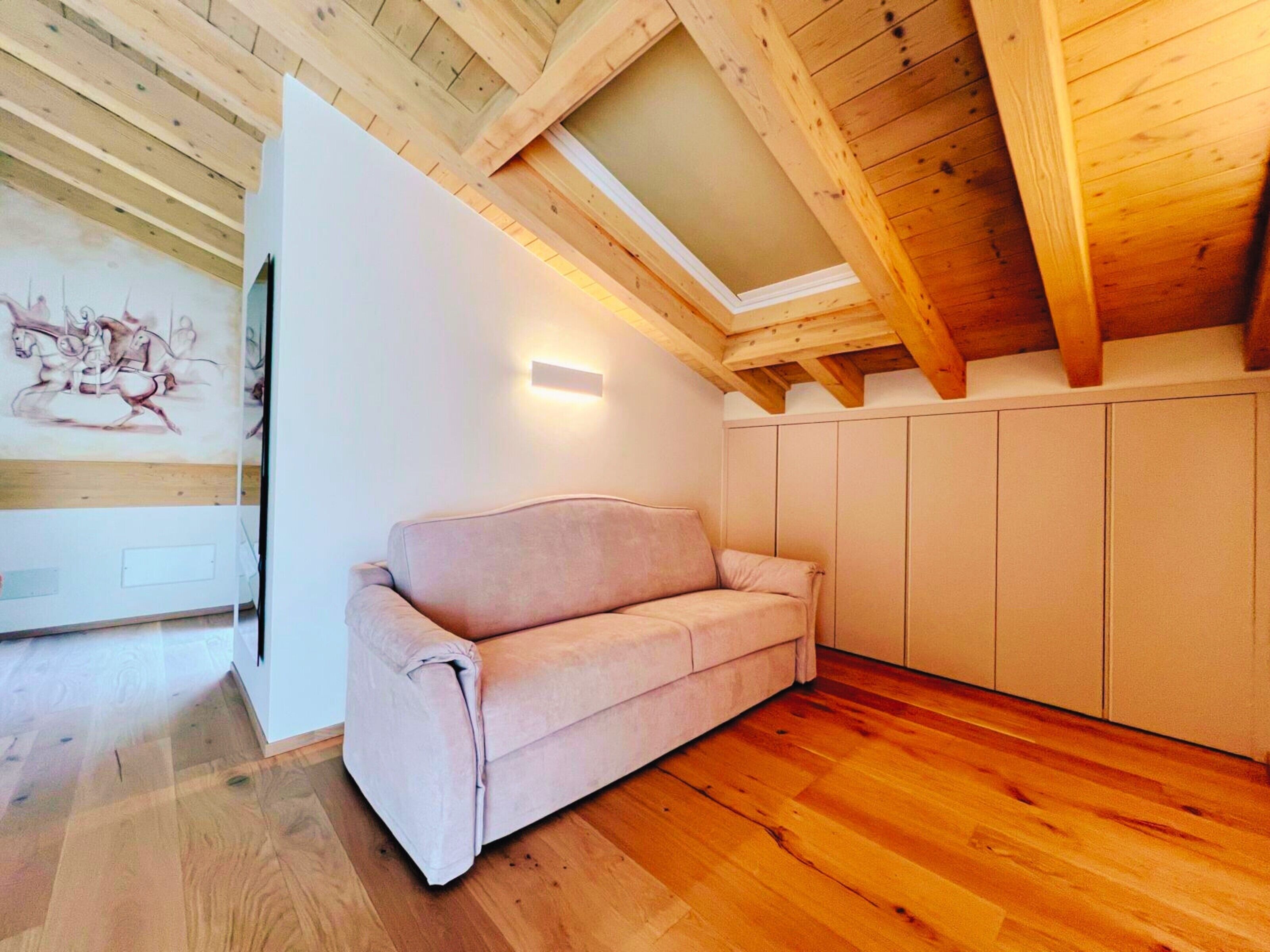 Una stanza moderna con soffitto in legno, un divano beige, una parete bianca con un lampadario e pavimento in legno.