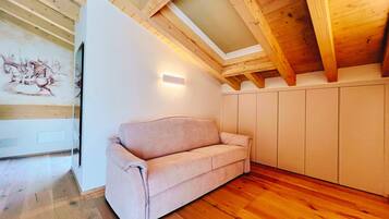 Una stanza moderna con soffitto in legno, un divano beige, una parete bianca con un lampadario e pavimento in legno.