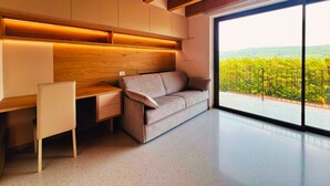 A modern interior with a sofa, a desk, and a large window offering a view of a vineyard. - 45 m² Soundproof Room with Private Bathroom and Terrace – Up to 4 Guests (Illasi)