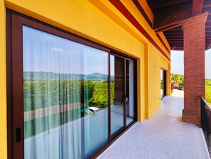 A modern building with large glass windows, a balcony, and a view of a green landscape.
