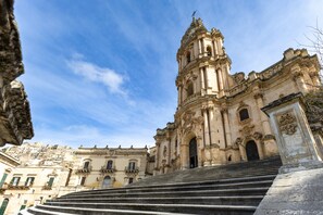 Un edificio histórico imponente con una torre de campanas destacada, una escalera que conduce a la entrada y detalles arquitectónicos clásicos.