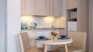 A compact kitchen with a dining area, featuring light wood cabinetry, a built-in microwave, and a dishwasher.