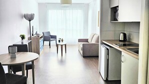 A modern, open-plan living and dining area with a kitchen, wooden flooring, and a large window with sheer curtains.