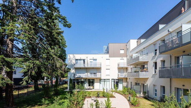 A modern multi-story residential building with balconies, a central courtyard, and surrounding greenery.