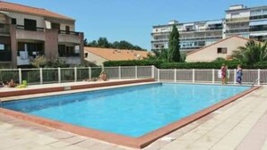 A swimming pool with a tiled deck, surrounded by a white fence, with buildings in the background. - Apartment 'Proche Mer' with Shared Pool, Wi-Fi and Air Conditioning (Argelès-sur-Mer)