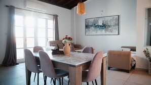 A modern dining area with a marble table, cushioned chairs, a vase of flowers, and a large abstract painting on the wall. - Lovely 1BR in Old Town: City Center & 4min to Beach (Larnaca)