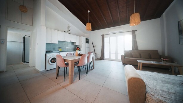 A modern kitchen with white cabinets, a dining table with chairs, a sofa, and a coffee table in a bright living area with a large window. - Lovely 1BR in Old Town: City Center & 4min to Beach (Larnaca)