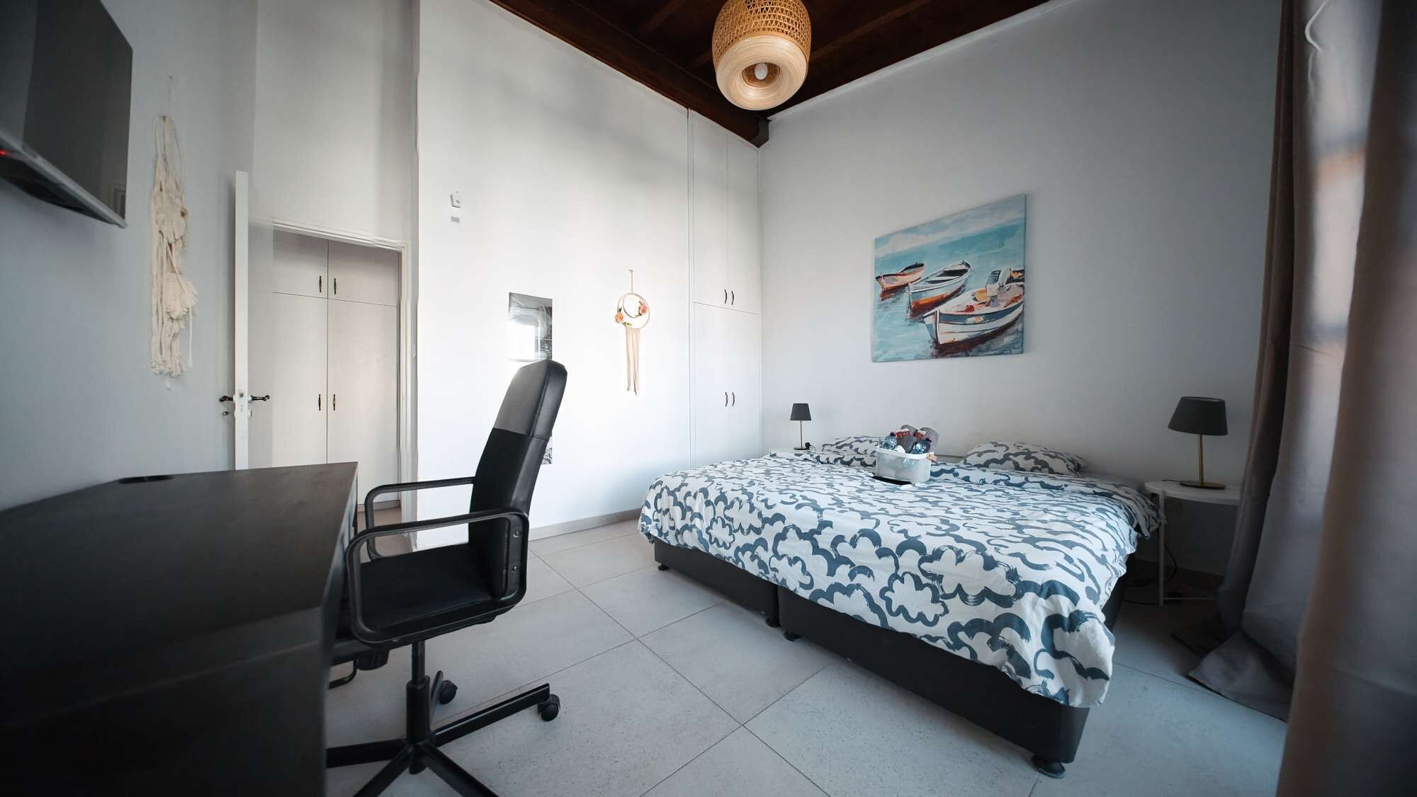 Een slaapkamer met een bed, bureau, stoel en een schilderij aan de muur.