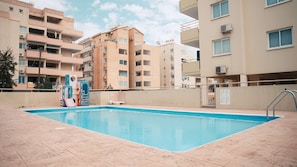 Una piscina amb una terrassa enrajolada, envoltada d'edificis de diversos pisos amb balcons i aparells d'aire condicionat.