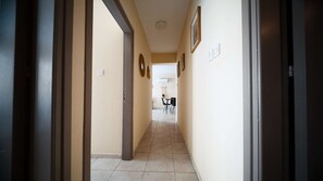 A hallway with a tiled floor, a door frame on the left, and a wall-mounted light switch.