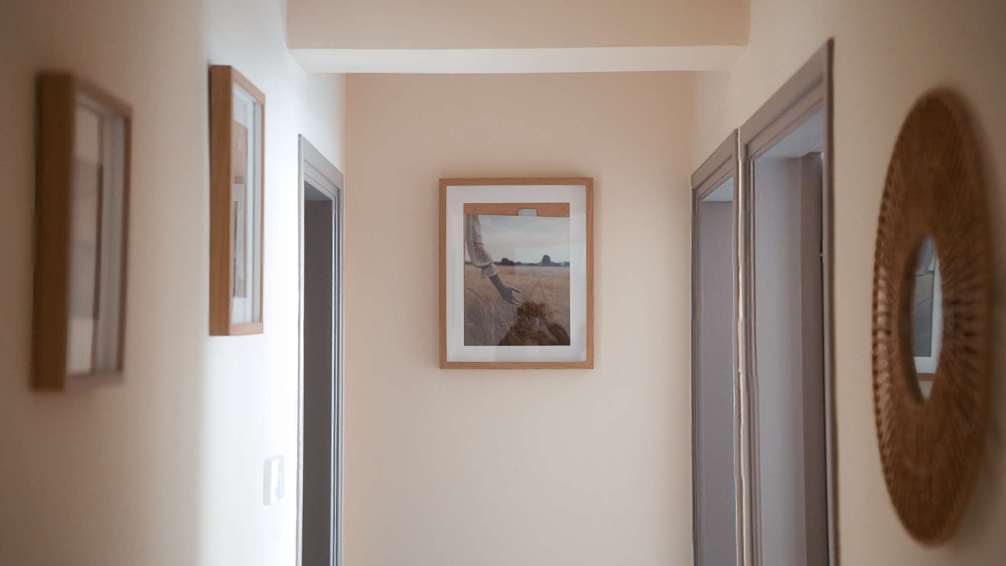 Een gang met ingelijste kunstwerken aan de wanden, een spiegel en deuren die naar andere kamers leiden.