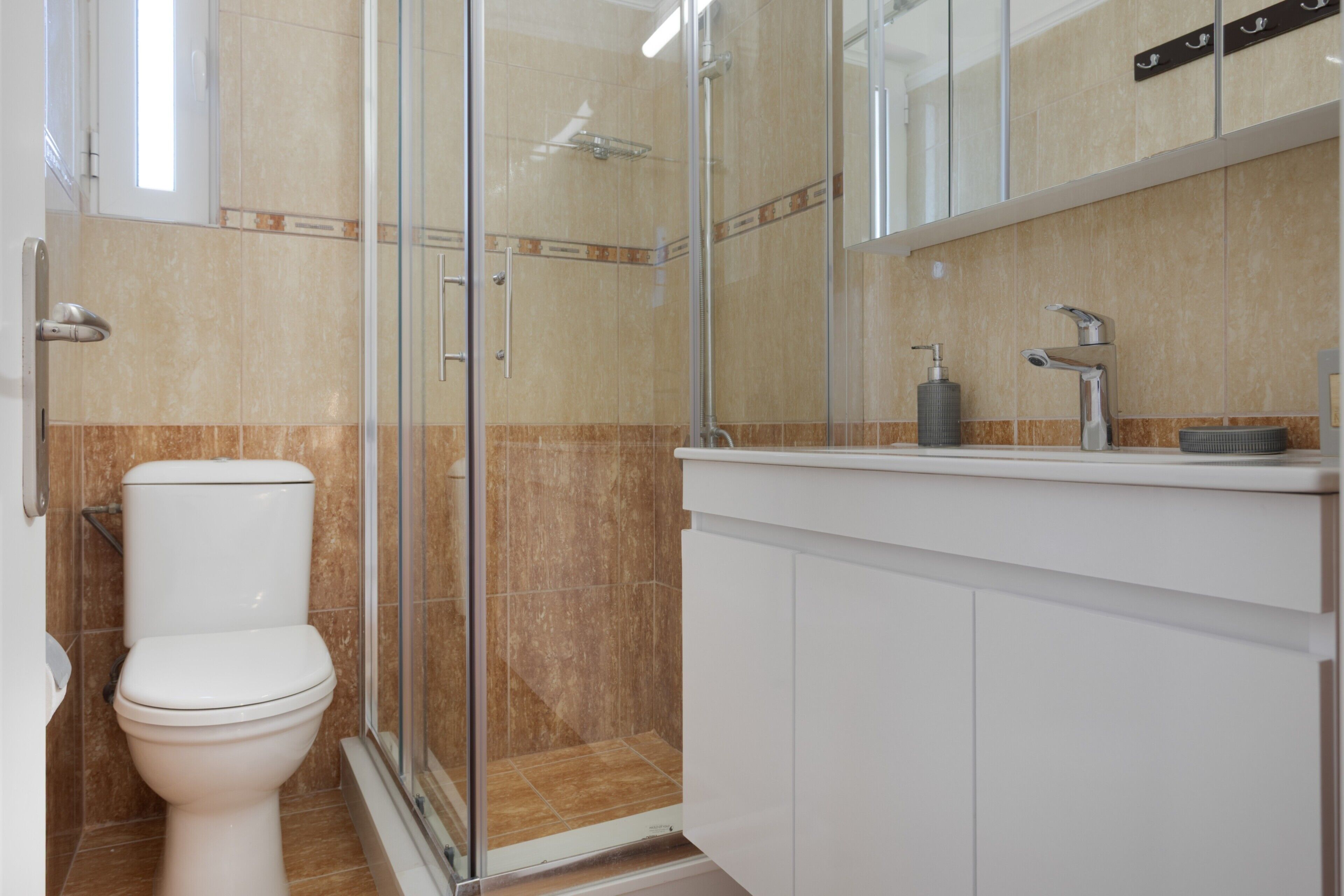 Un baño moderno con ducha de vidrio, inodoro blanco y lavamanos con dispensador de jabón.