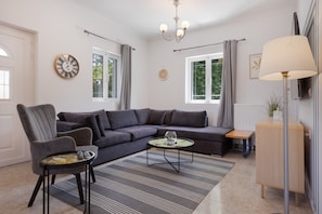 Un salon moderne avec un canapé d’angle, une petite table ronde, un fauteuil, une lampe sur pied et une horloge murale.