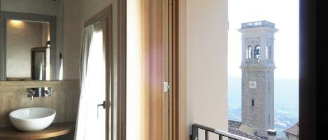 A bathroom with a wooden vanity, a white sink, and a large window overlooking a tower.