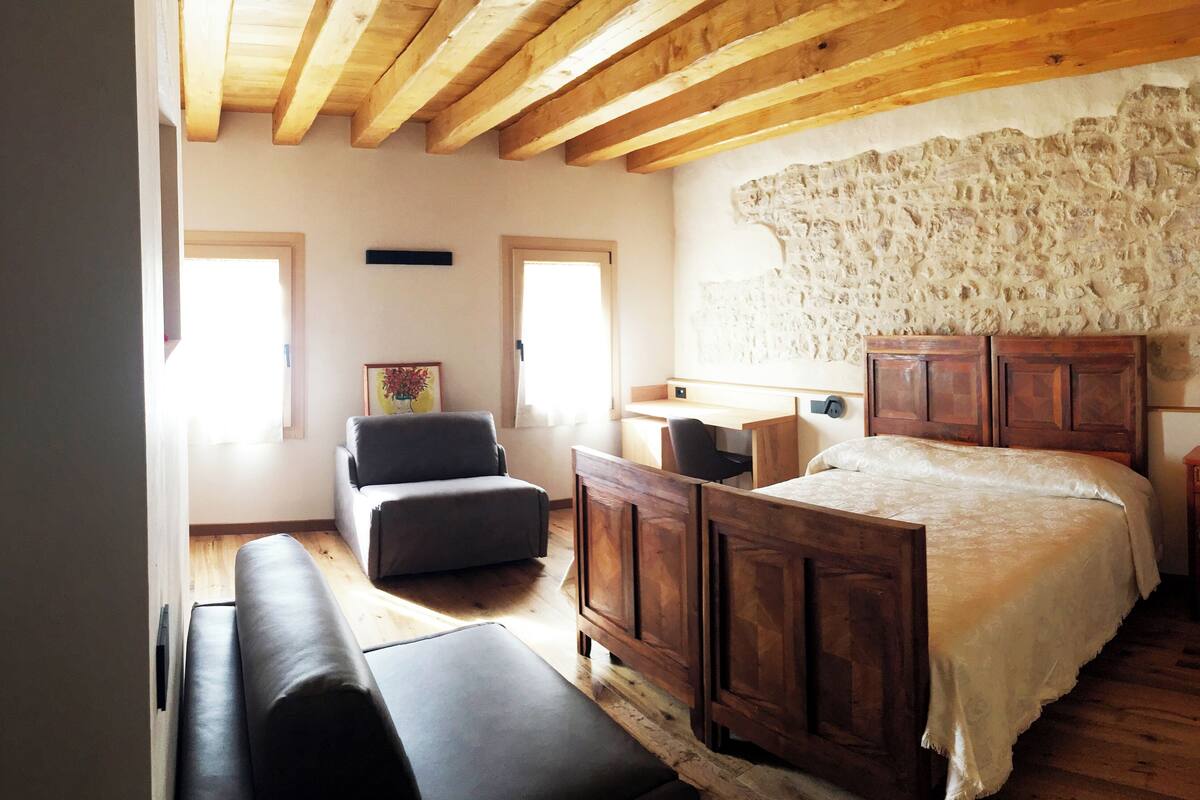 Une chambre avec un mur en pierre, un lit en bois, un banc, un bureau et une chaise.