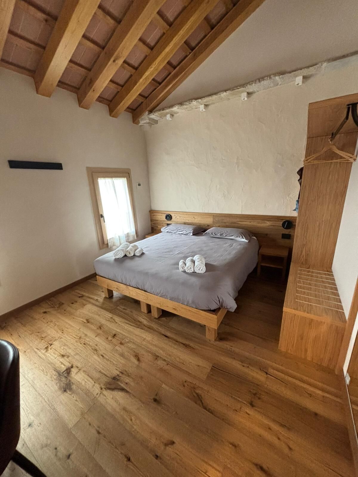 Une chambre avec un lit en bois, un plancher en bois, un plafond en pente et un petit banc en bois.
