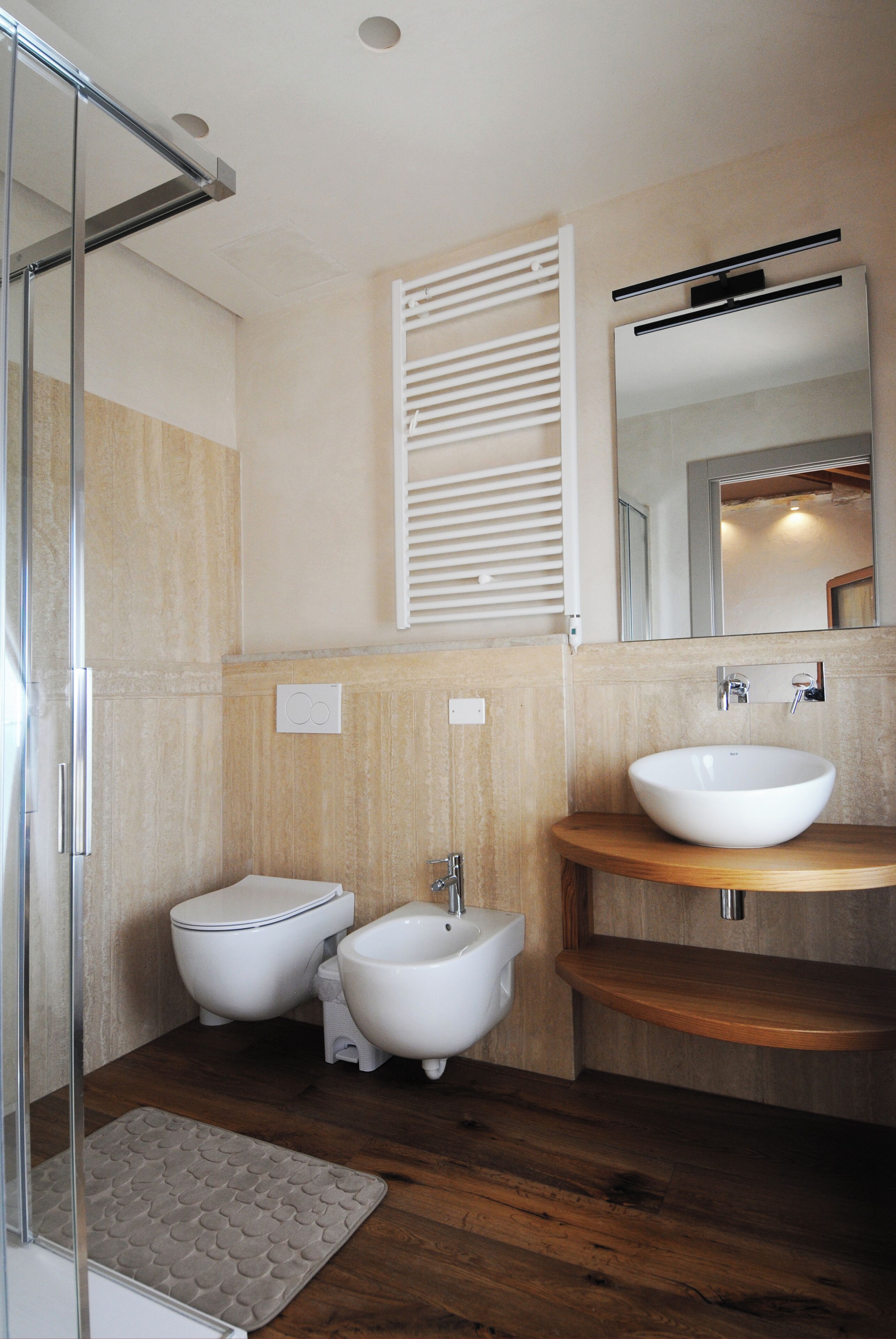 Une salle de bain dotée d’une douche à parois de verre, de deux toilettes, d’un bidet, d’un meuble-lavabo en bois avec un évier et d’un miroir au-dessus du meuble-lavabo.