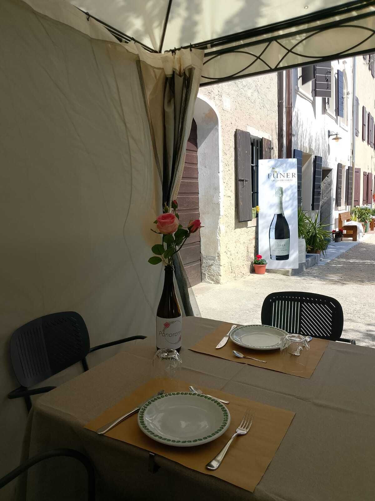 Mesa preparada para dos, con una botella de vino, un florero con flores y un cartel publicitario de vino.