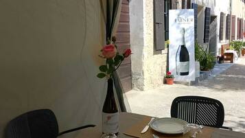 Mesa preparada para dos, con una botella de vino, un florero con flores y un cartel publicitario de vino.