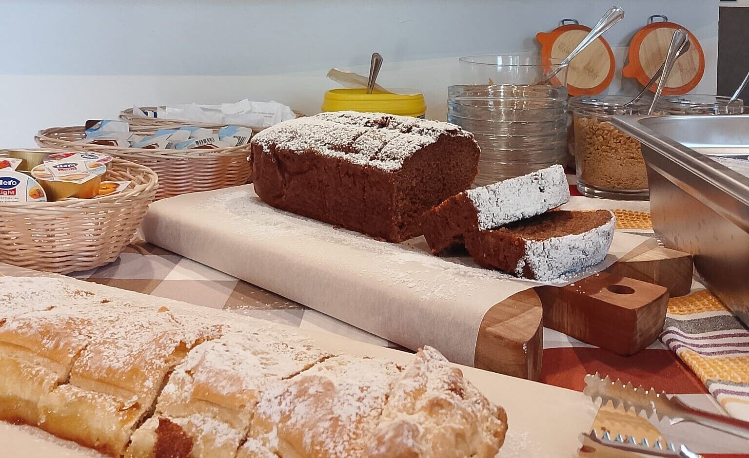 A buffet table with various baked goods, including bread and pastries, and serving utensils.
