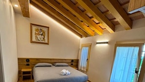 A bedroom with a wooden ceiling, a bed with a grey mattress, a bedside table, and a painting on the wall.