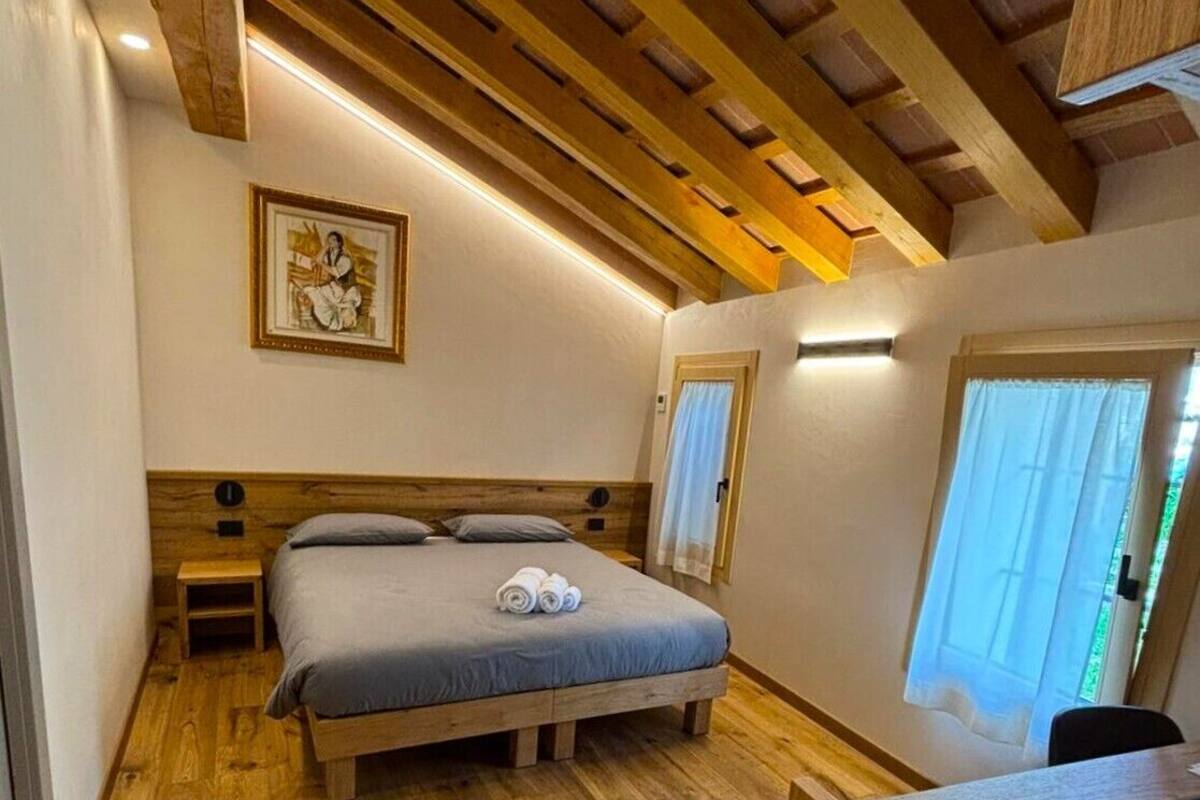 Une chambre avec un plafond en bois, un lit doté d’un matelas gris, une table de chevet et un tableau accroché au mur.
