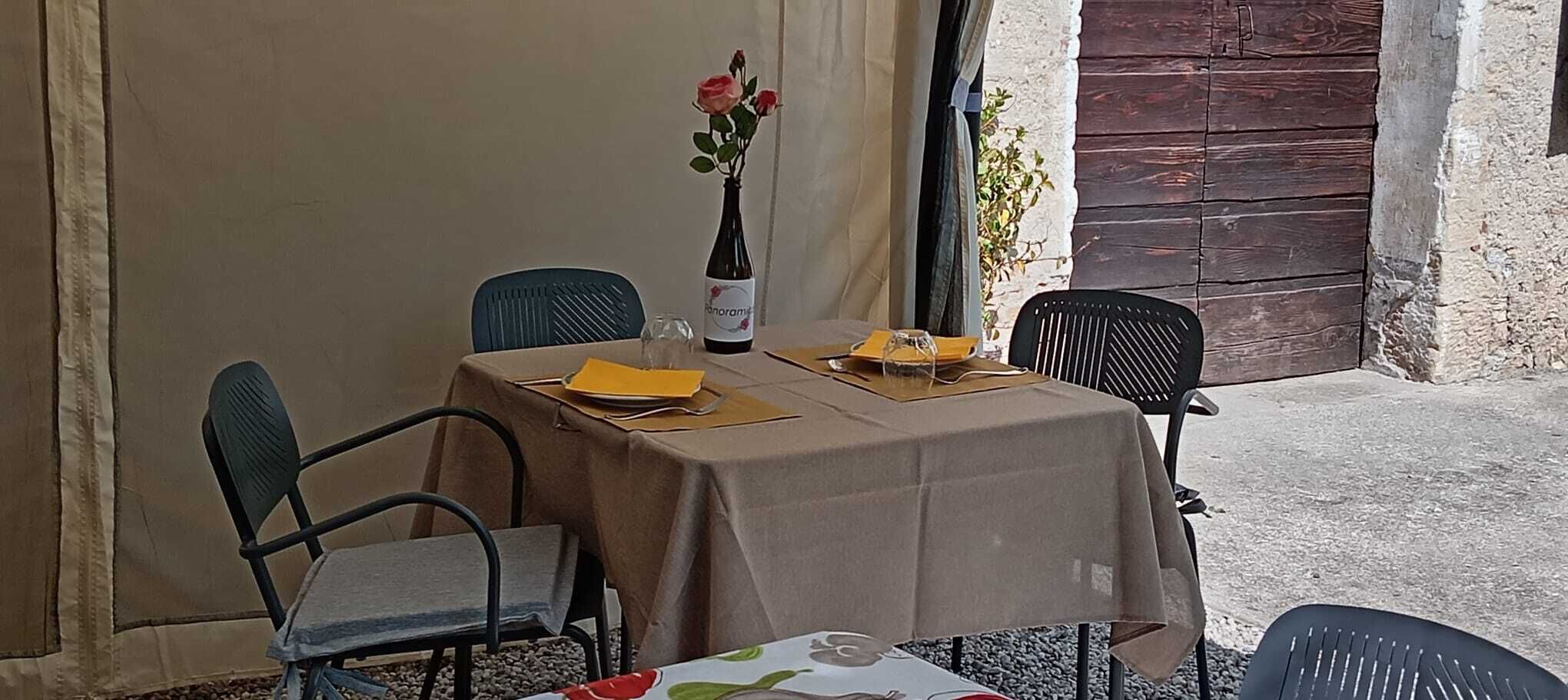 Une table dressée pour deux personnes, avec une bouteille de vin, un vase de fleurs et un menu.