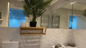A modern bathroom with a marble floor, a white bathtub, a toilet, and a shelf with a potted plant. - Apartment 07 St Andrews (Lytham St. Anne's)