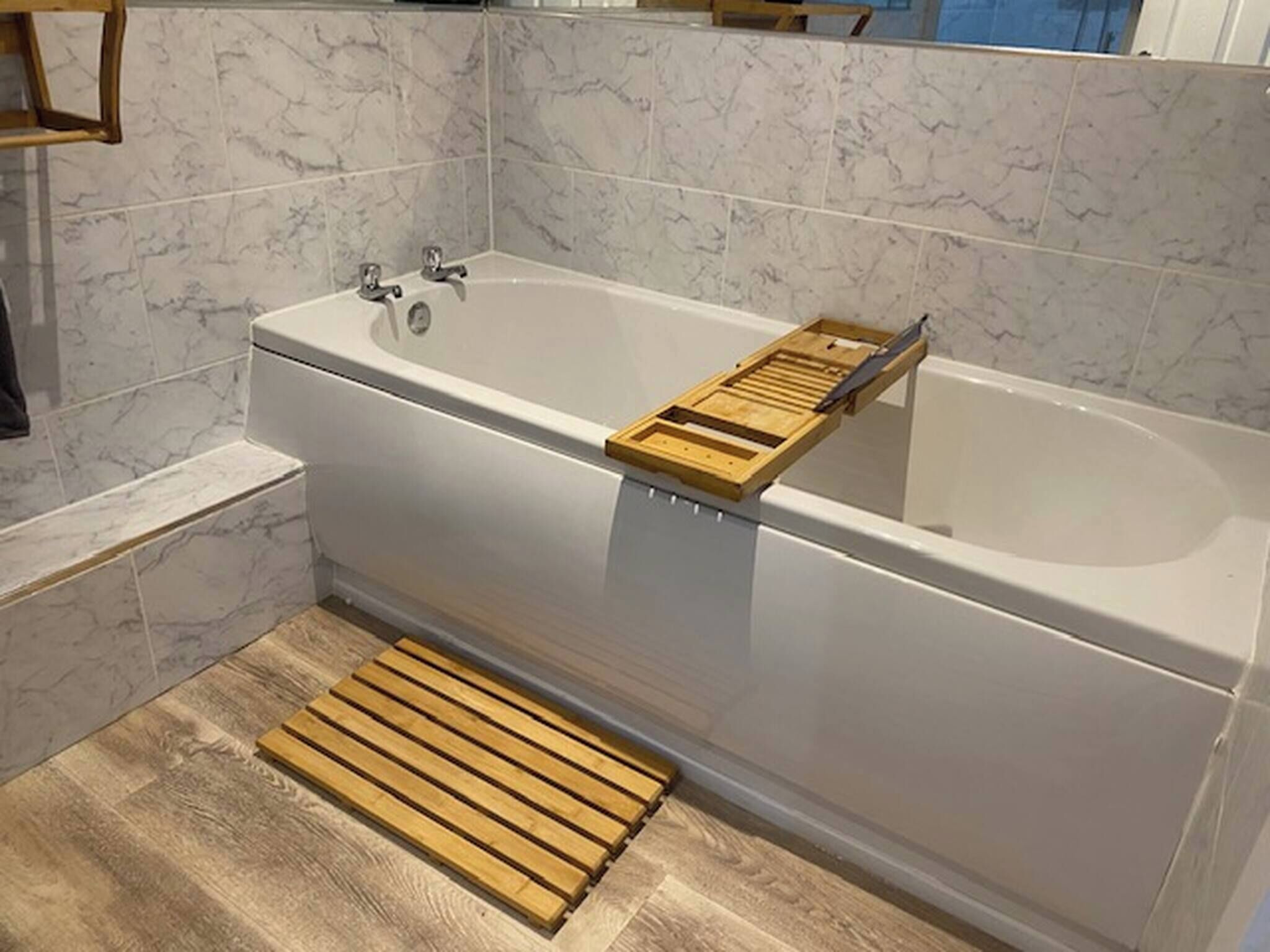 A modern bathroom with a freestanding bathtub, wooden bath mat, and marble tiles.
