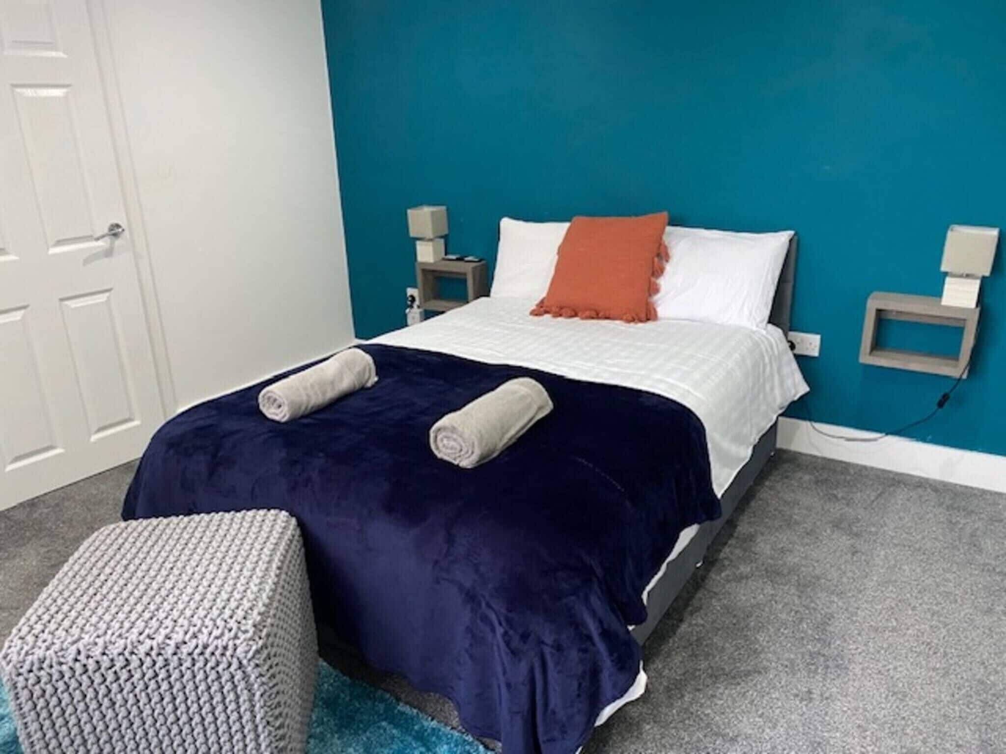 A bedroom with a bed, a blue wall, a white door, and a grey carpet.