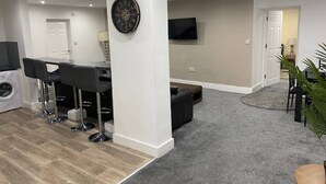 A modern living room with a dining area, a TV mounted on the wall, and a washing machine in the corner. - Apartment 07 St Andrews (Lytham St. Anne's)