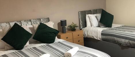 A hotel room with two beds, striped bedding, green pillows, and a nightstand with a lamp and a plant.