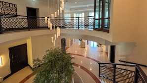 Un hall d’entrée spacieux avec un plafond haut, un éclairage moderne suspendu, un escalier central et une grande fenêtre laissant entrer la lumière naturelle.
