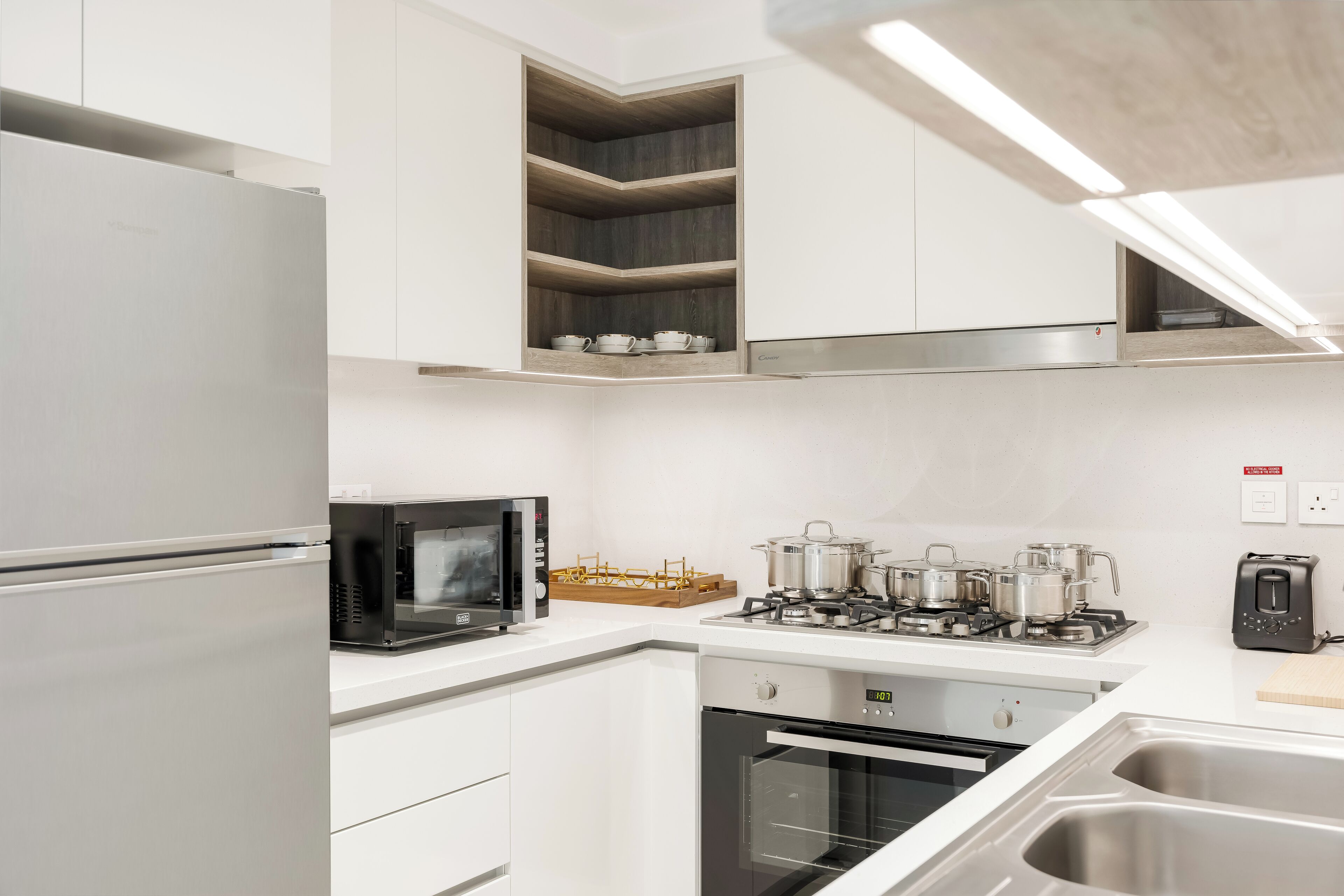 Une cuisine moderne avec des meubles blancs, un four à micro-ondes encastré, une cuisinière à gaz et un évier en acier inoxydable.