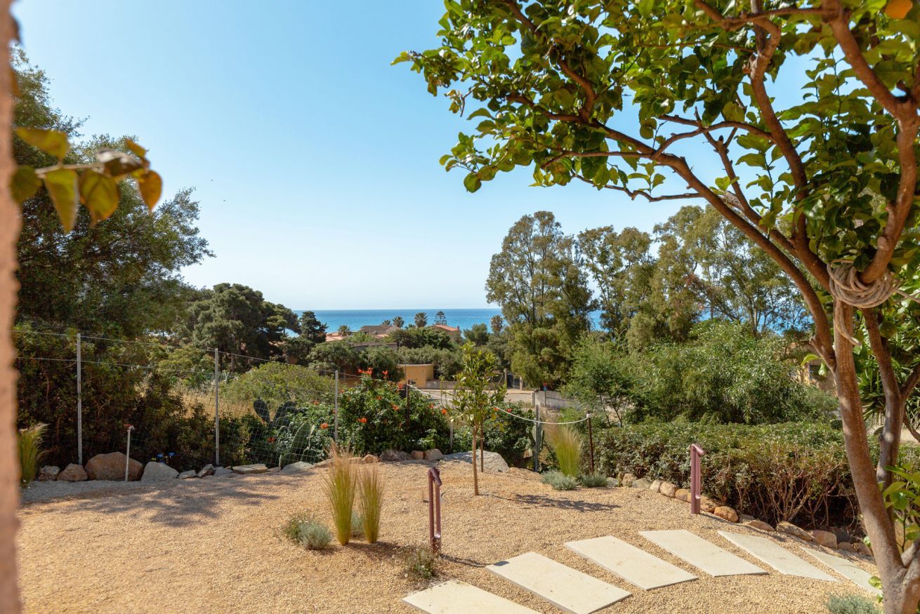 Un jardín con un sendero de grava, árboles y vistas al mar.