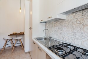 Cozinha com fogão a gás, pia de aço inoxidável, banquetas de madeira e painel de fundo estampado.