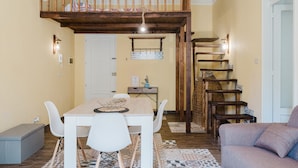 A dining area with a wooden table and chairs, a bench, a staircase with a wooden railing, and a wall-mounted shelf with decorative items.