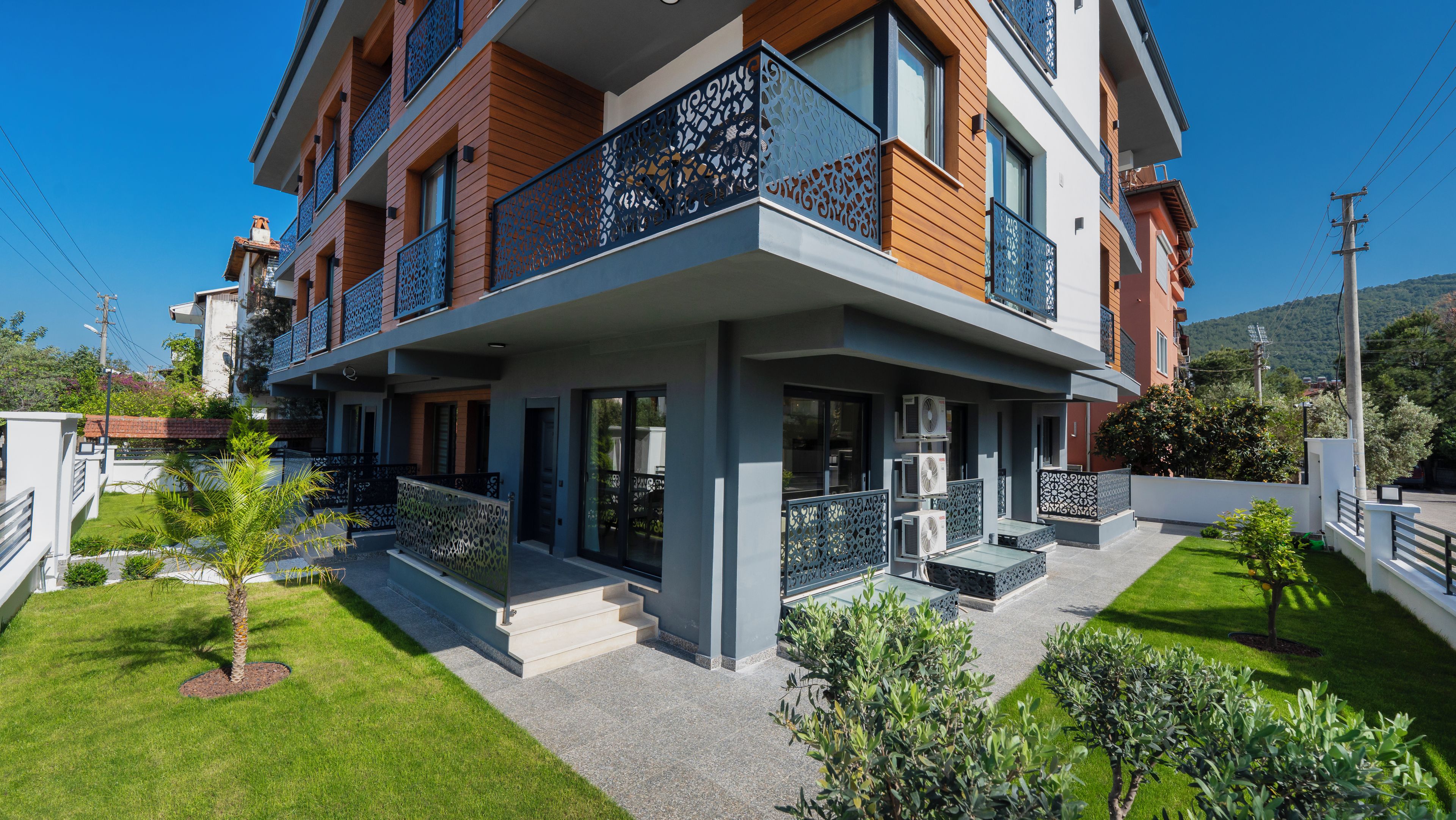 A multi-story residential building with balconies, a covered entrance, and a well-maintained lawn.