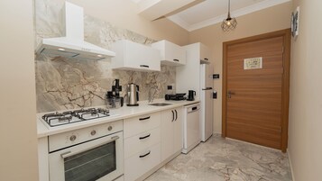 Una cocina moderna con estufa a gas, horno, armarios blancos y una salpicadera de mármol.